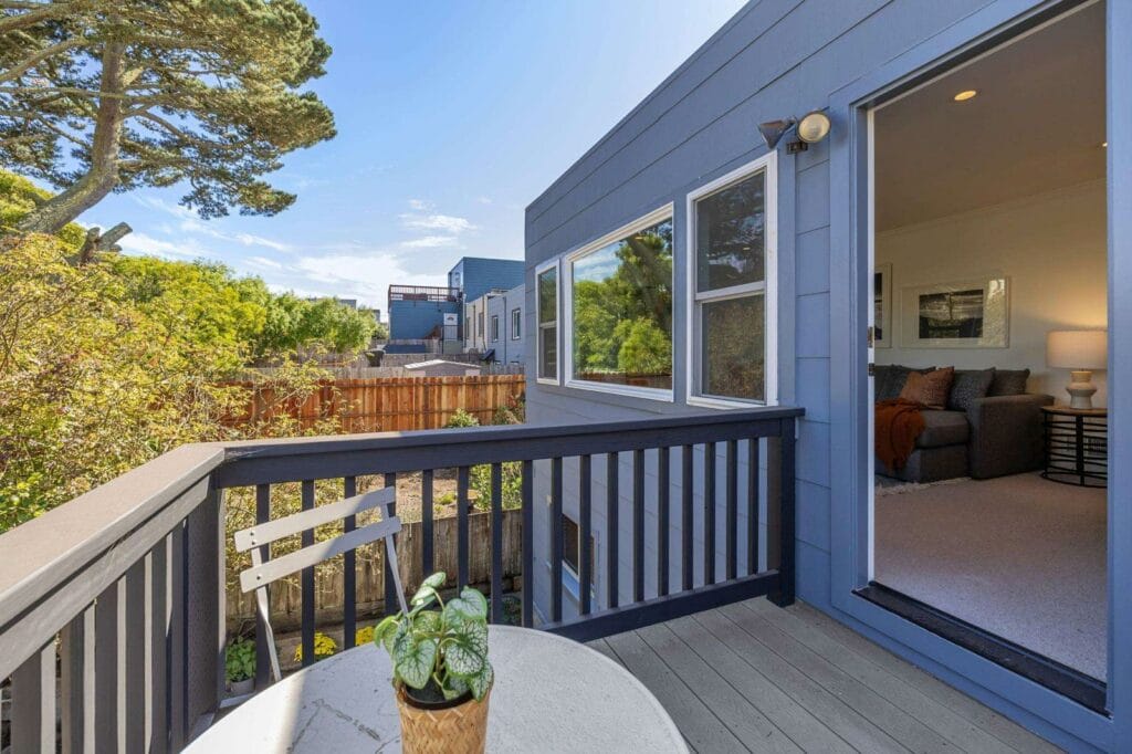 A cozy backyard deck with a small table and chair, next to an open door leading to a living room.